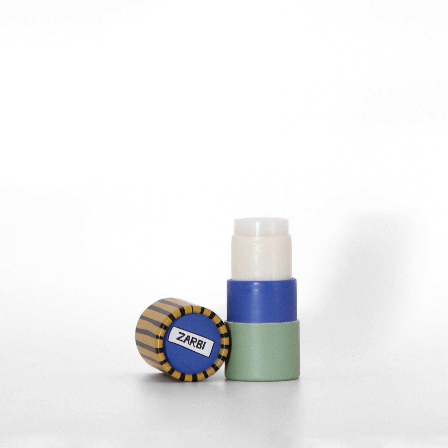 Open twist-up Jasmine Green Tea lip balm tube with mint base showing clear balm inside. Yellowish green cap with black stripes laying on the side with blue top showing Zarbi logo.
