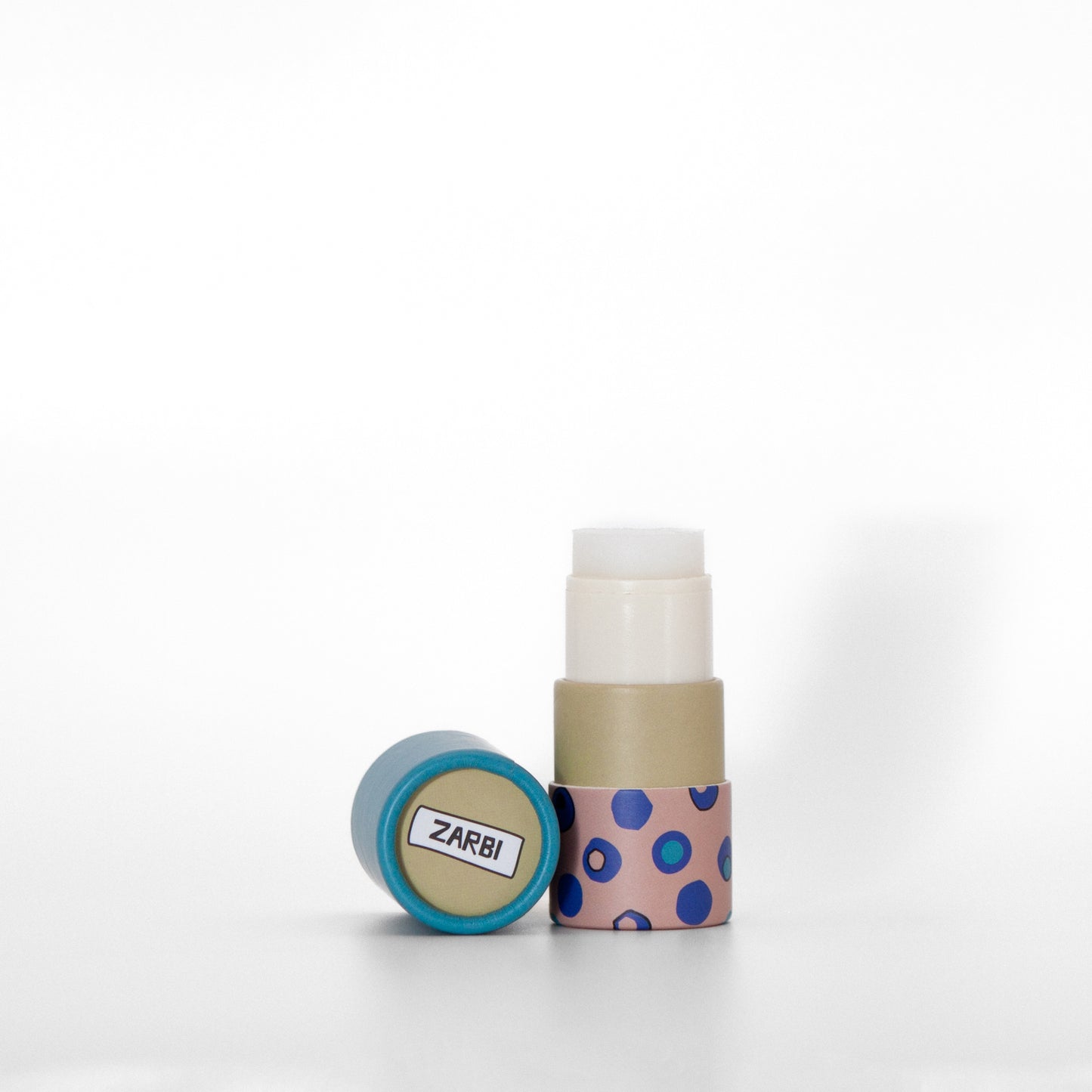 Open twist-up Verbena lip balm tube with pink base, irregular blue circle pattern showing clear balm inside. Light blue cap laying on the side with khaki top showing Zarbi logo.