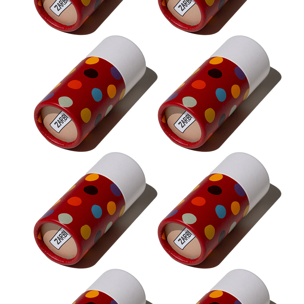 Flat lay of Zarbi vegan lip balms with bold red tubes and colorful polka dot patterns, arranged diagonally on a white background with harsh shadows.