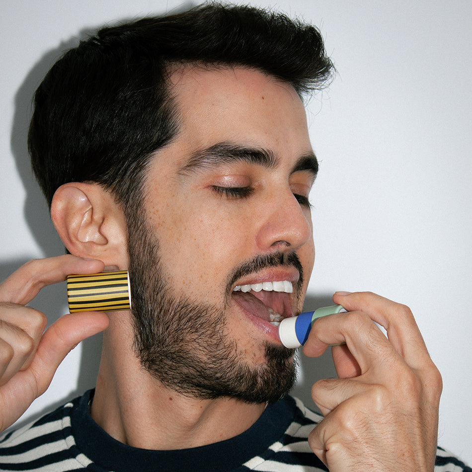 Man applying Zarbi vegan lip balm while holding a striped cap near his face, showcasing a bold and fun lip care moment.
