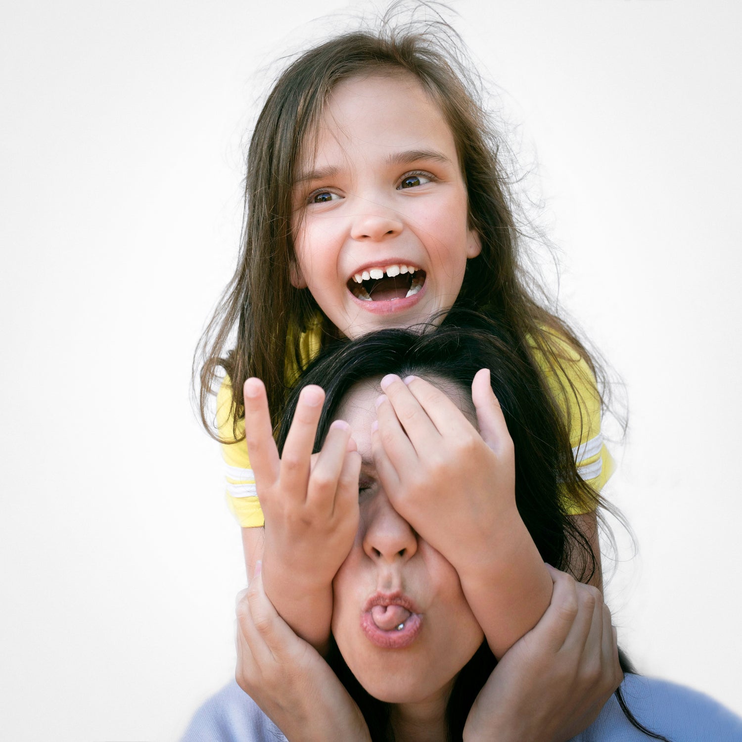 A young girl playfully covers the eyes of a woman while laughing, creating a joyful and candid moment.