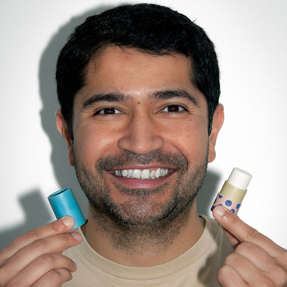 Smiling man holding a Zarbi vegan lip balm tube, showcasing colorful packaging and joyful self-care.
