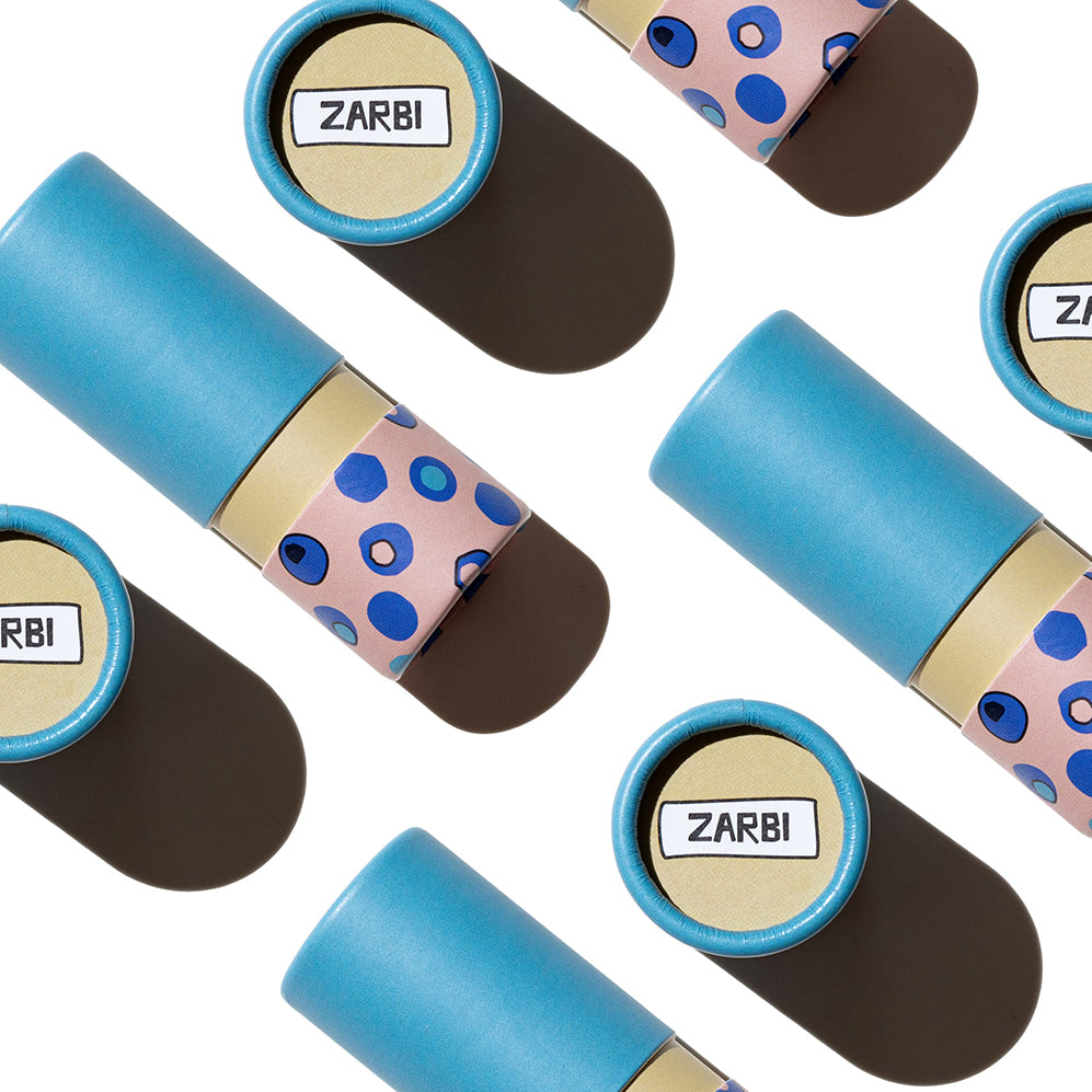 Flat lay of Zarbi vegan lip balms with vibrant blue caps and playful polka-dot packaging, arranged on a light background with bold shadows.