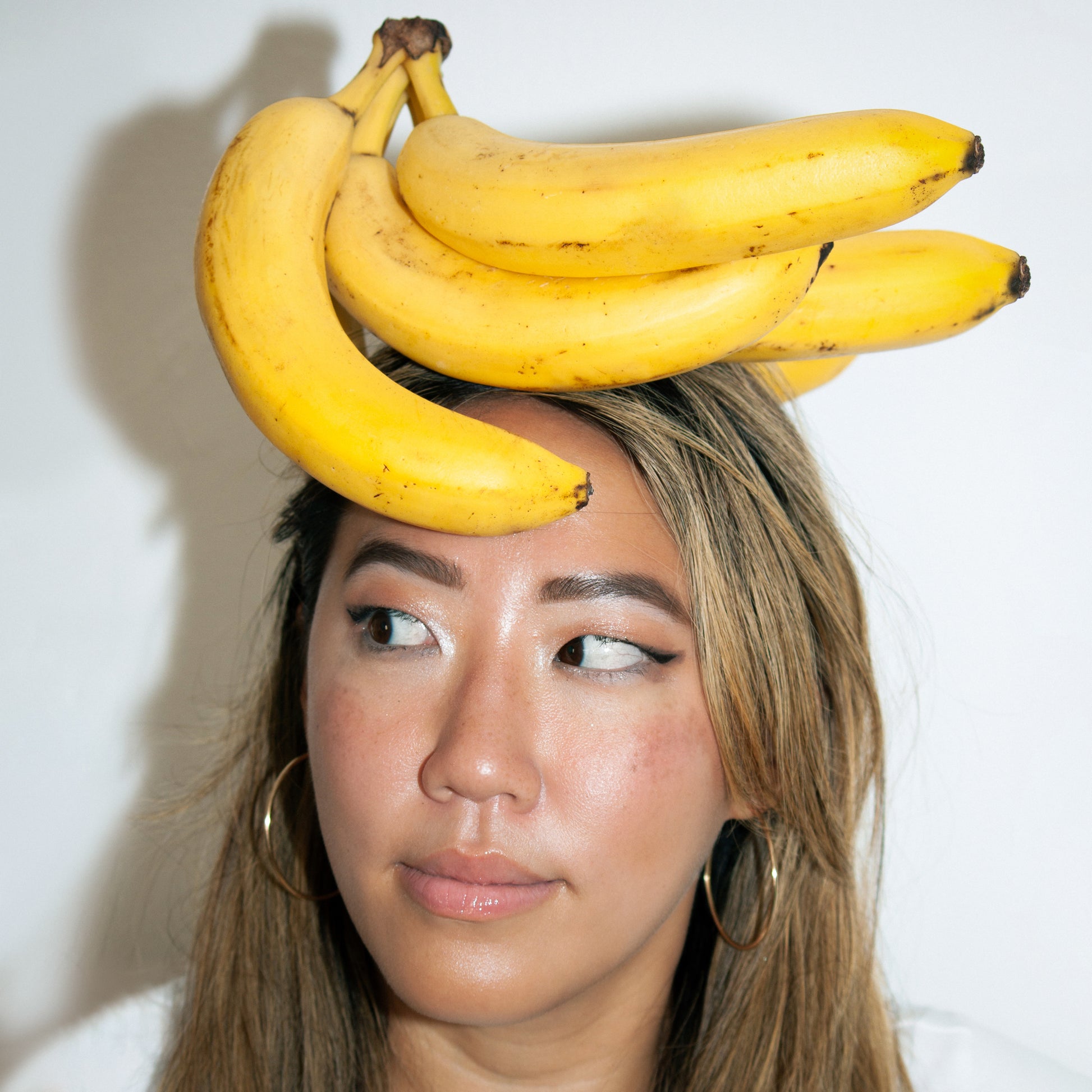 Asian girl with bunch of ripe yellow bananas on top of head.