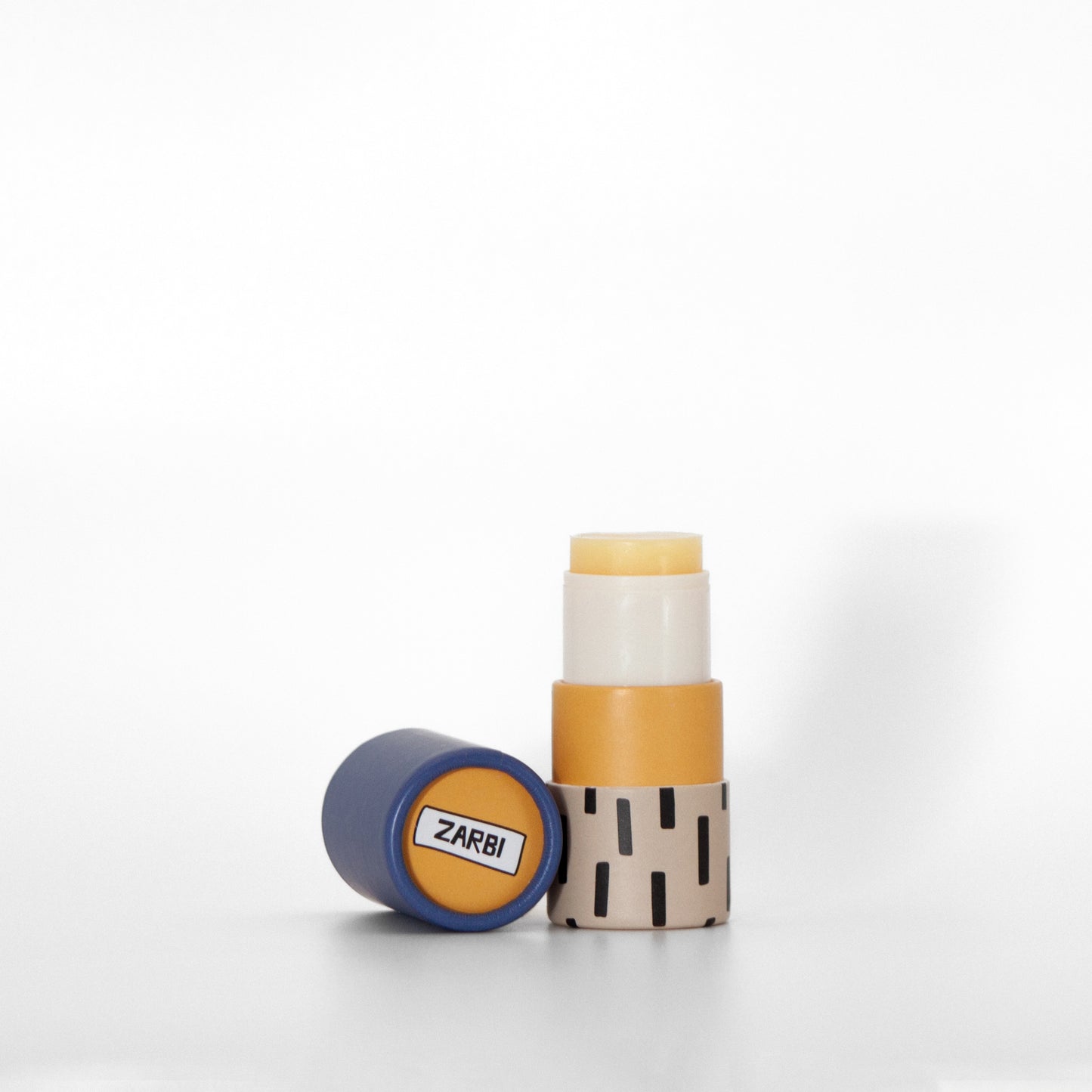 Open twist-up Sea Buckthorn lip balm tube with tan base, black irregular rectangle pattern showing yellow balm inside. Blue cap laying on the side with orange top showing Zarbi logo.