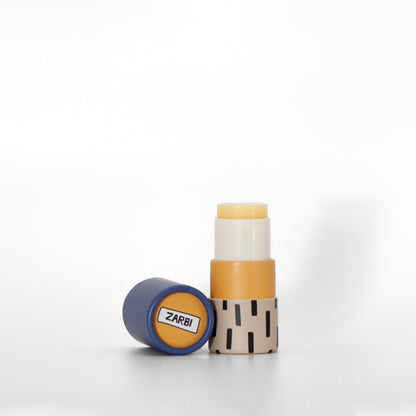 Open twist-up Sea Buckthorn lip balm tube with tan base, black irregular rectangle pattern showing yellow balm inside. Blue cap laying on the side with orange top showing Zarbi logo.