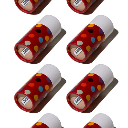 Flat lay of Zarbi vegan lip balms with bold red tubes and colorful polka dot patterns, arranged diagonally on a white background with harsh shadows.