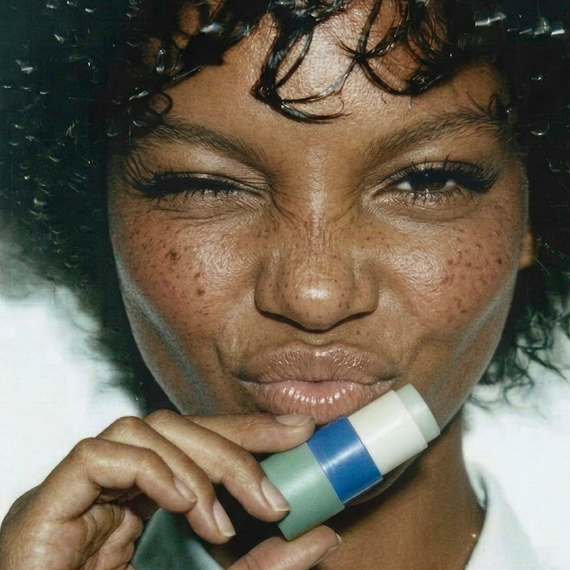 Model holding Zarbi Jasmine Green Tea vegan lip balm in green and blue paper packaging.