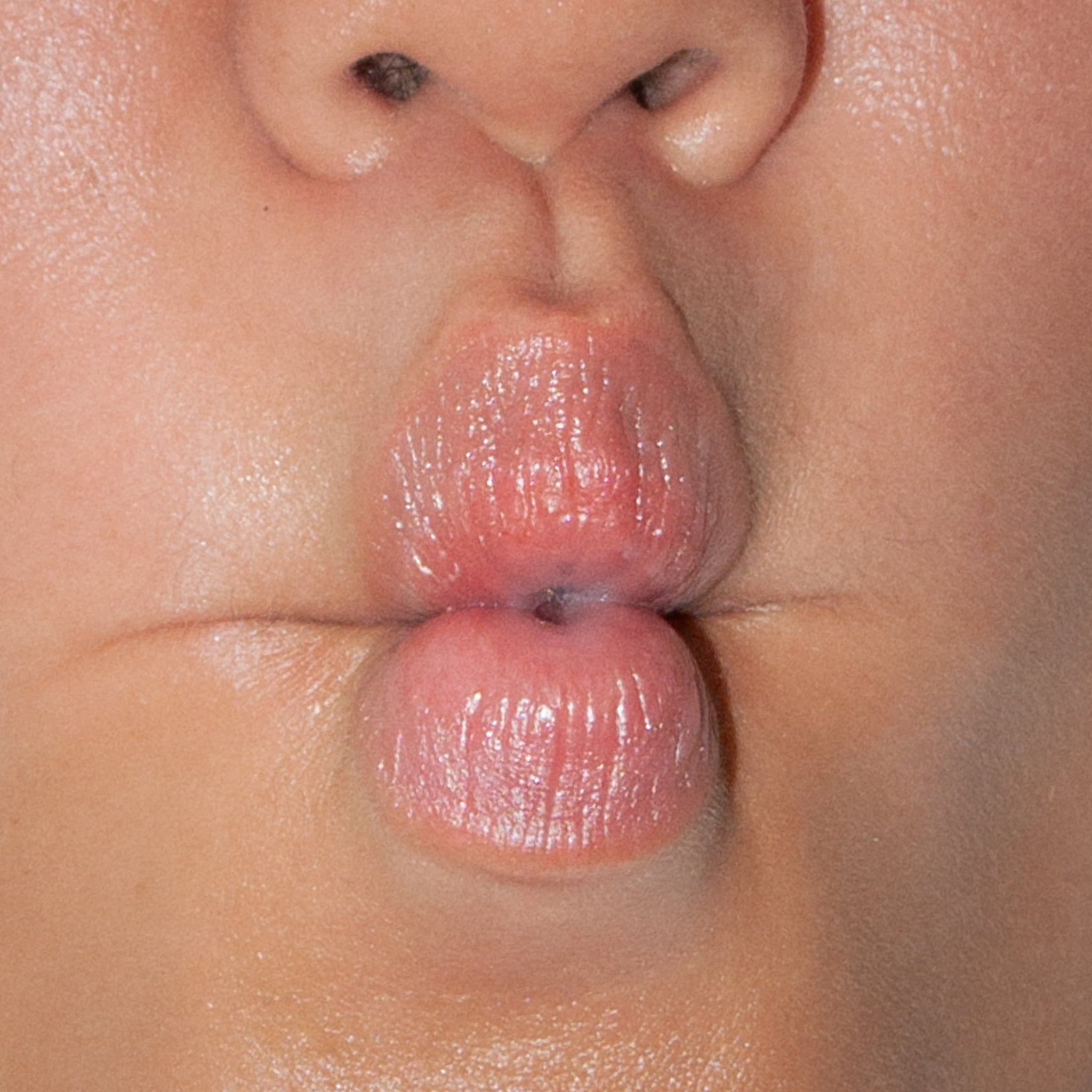 A close-up of glossy puckered lips making a kissy face, highlighting natural texture and shine.